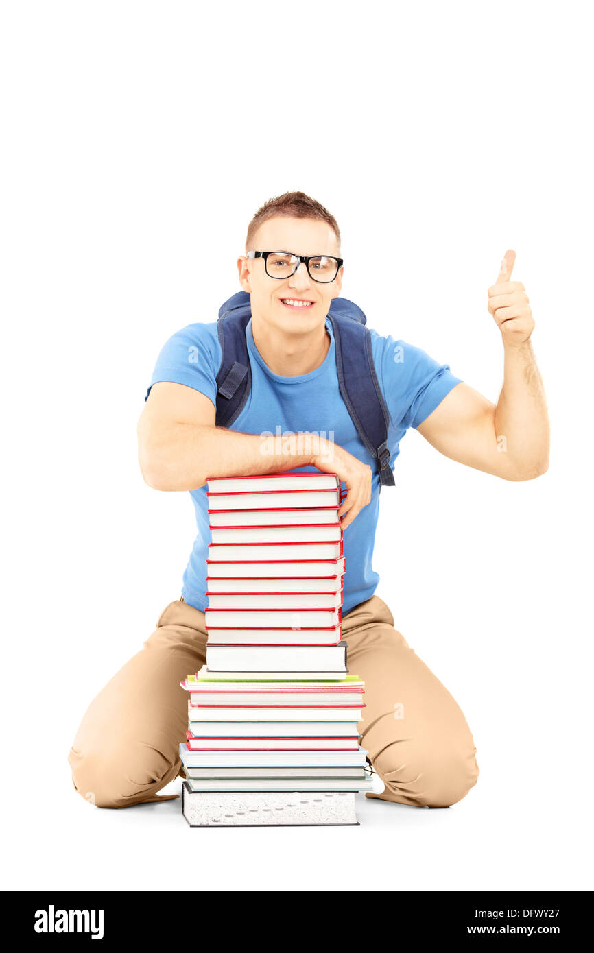 Smiling male student with school bag on a pile of books giving thumb up ...