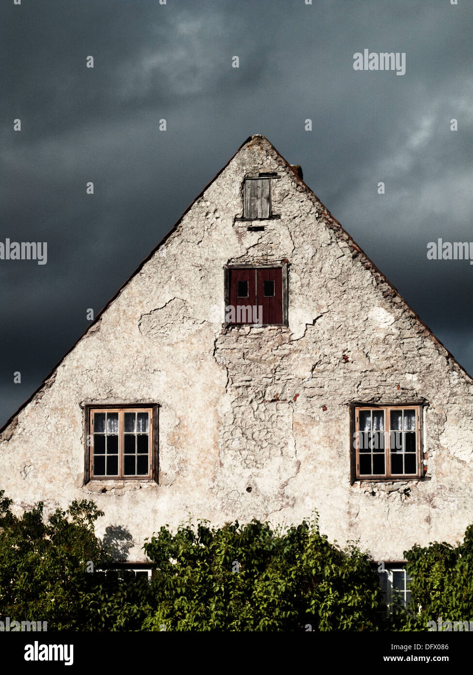 Profile of Old Rustic Cottage with Sloping Roof Against Ominous Gray Sky Stock Photo