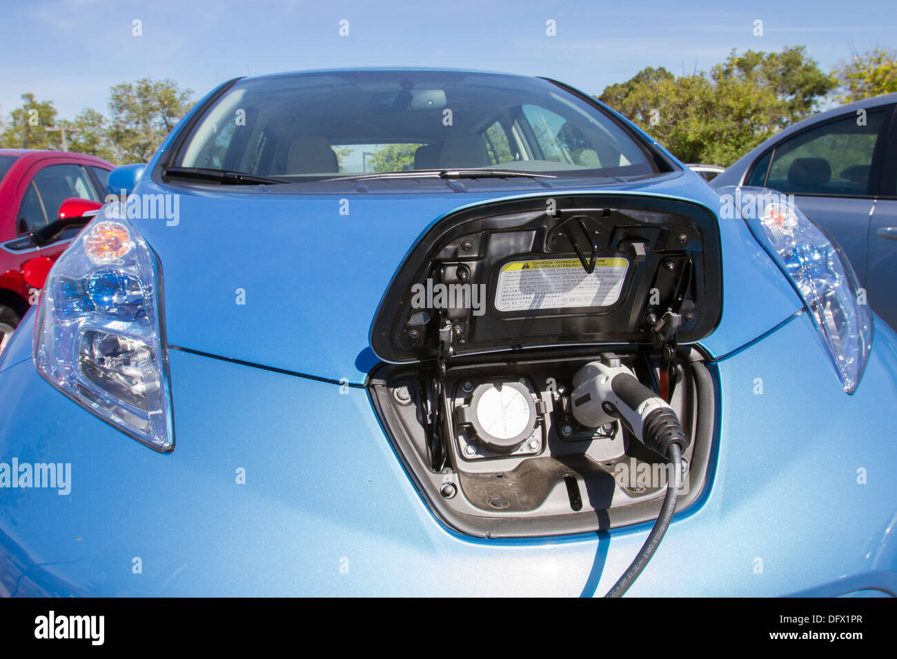 Blue plug-in electric car with connector plugged into a charging station to charge its battery in a company parking lot Stock Photo