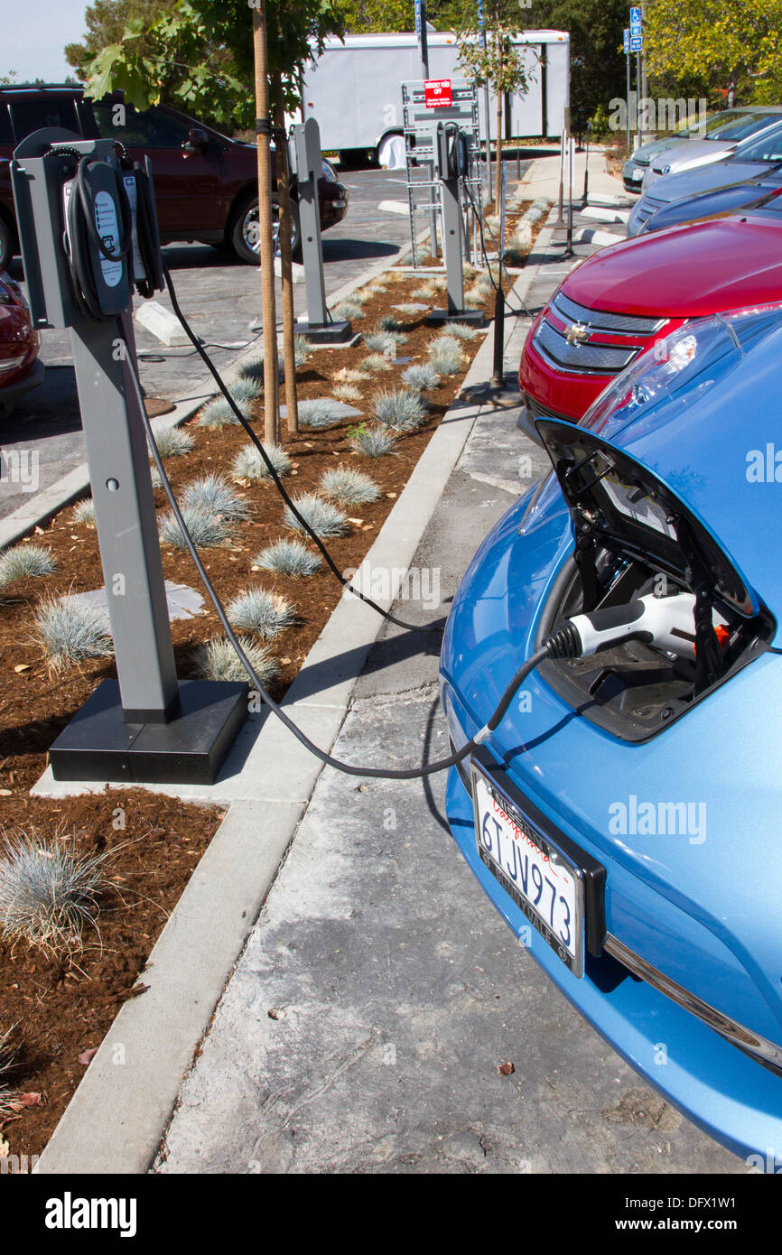 Plug-in electric cars plugged into an EV charging station to charge their batteries in a workplace parking lot Stock Photo