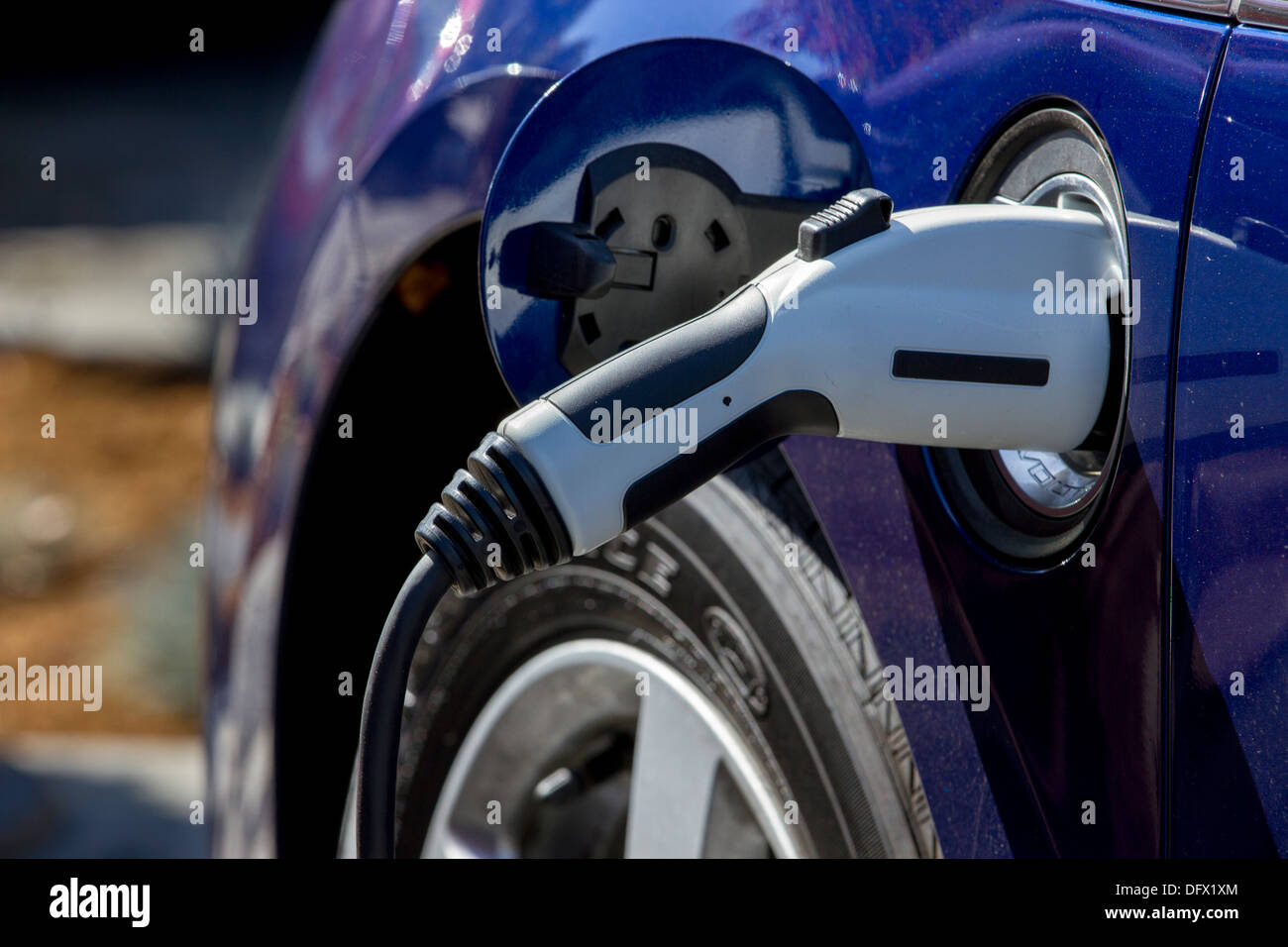 Blue plug-in electric car with connector plugged into a charging station to charge its battery in a company parking lot Stock Photo