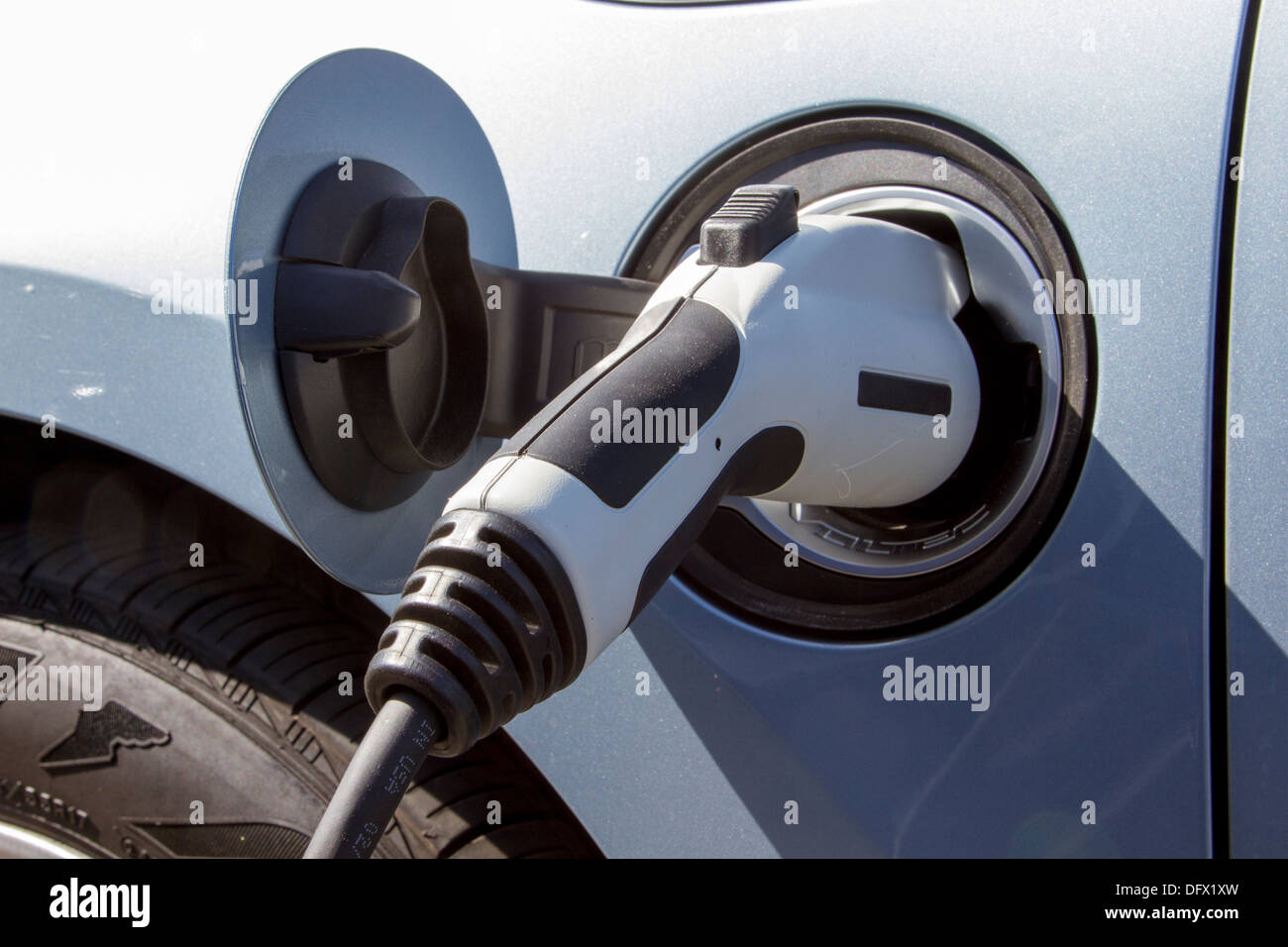 Plug-in electric car with connector plugged into a charging station to charge its battery in a company parking lot Stock Photo