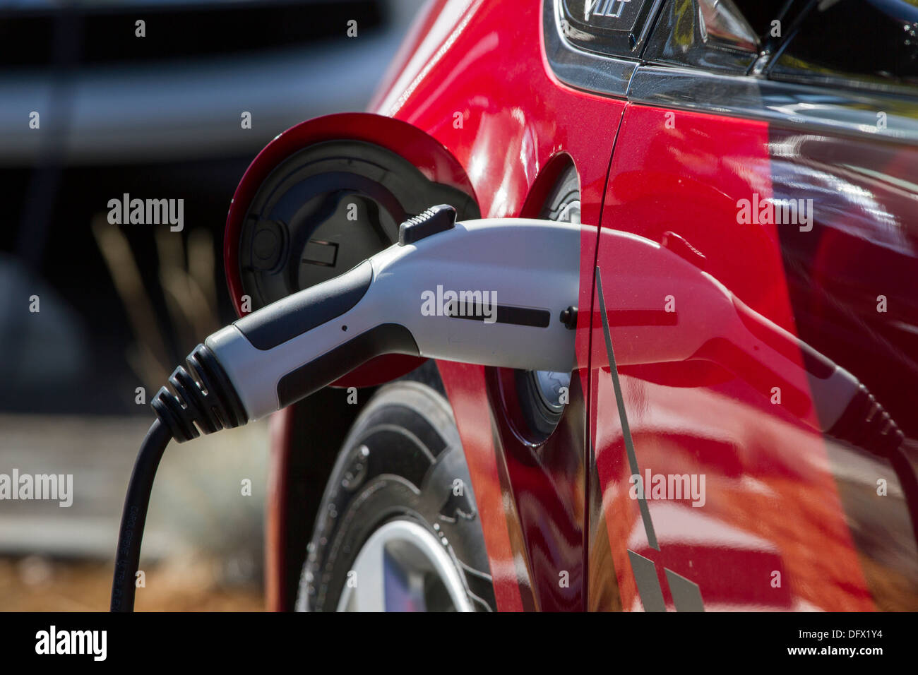 Red plug-in electric car with connector plugged into a charging station to charge its battery in a company parking lot Stock Photo