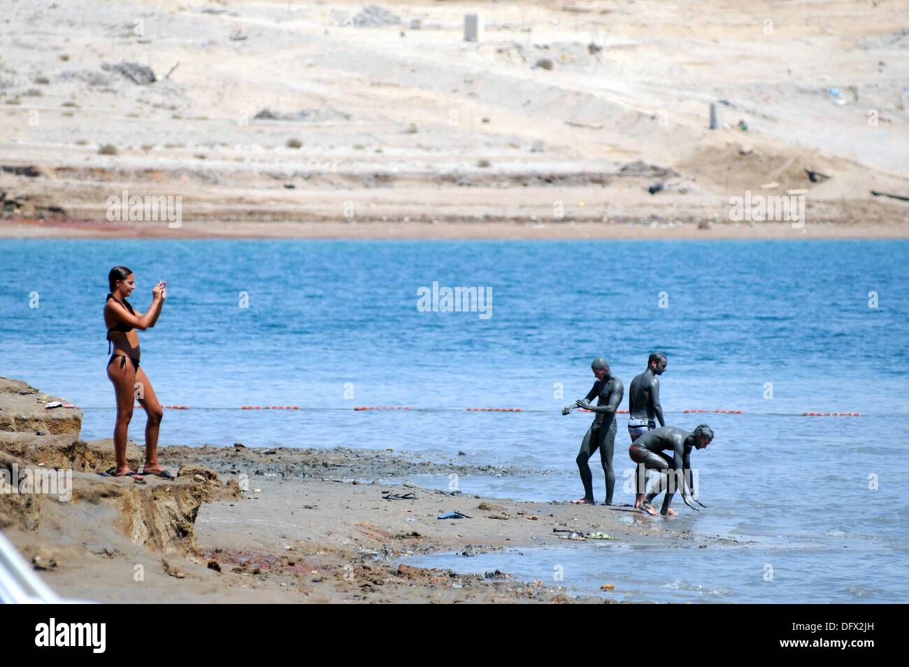 Three young men cover themselves in mud from the Dead Sea and a young woman takes pictures in Israel, 11 September 2013. The Dead Sea, bordering Israel and Jordan, is famous for its high salinity of about 30% (around ten times more than the Mediterranean Sea) that easily carries the human body. Its water source is the River Jordan and it does not have an outlet; healing powers for atopic dermatitis and psioriasis are attributed to its water and mud. This is reason, health tourism has developed at different places of the Dead Sea. The whole area of the Dead Sea lies 416 meters below sea level. Stock Photo