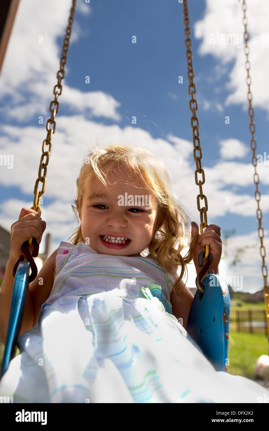 Little toddler girl on the swing having great time, holding the chain