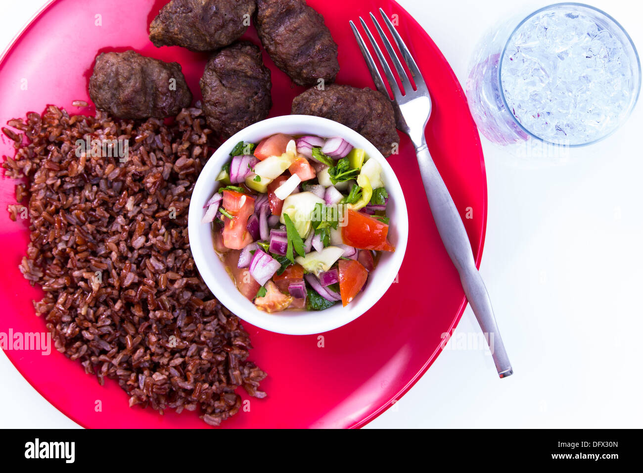 Turkish Meat Balls Kofte served with Red Rice Pilaf and Turkish Shepperd Salad on a red plate along with ice water. Isolated on Stock Photo