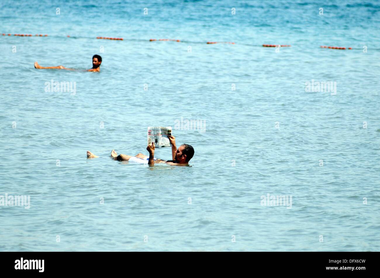 Reading the newspaper in the Dead Sea - a popular photograph subject, in Israel, 11 September 2013. The Dead Sea, bordering Israel and Jordan, is famous for its high salinity of about 30% (around ten times more than the Mediterranean Sea) that easily carries the human body. Its water source is the River Jordan and it does not have an outlet; healing powers for atopic dermatitis and psioriasis are attributed to its water and mud. This is reason, health tourism has developed at different places of the Dead Sea. The whole area of the Dead Sea lies 416 meters below sea level. Photo: Matthias Tödt Stock Photo