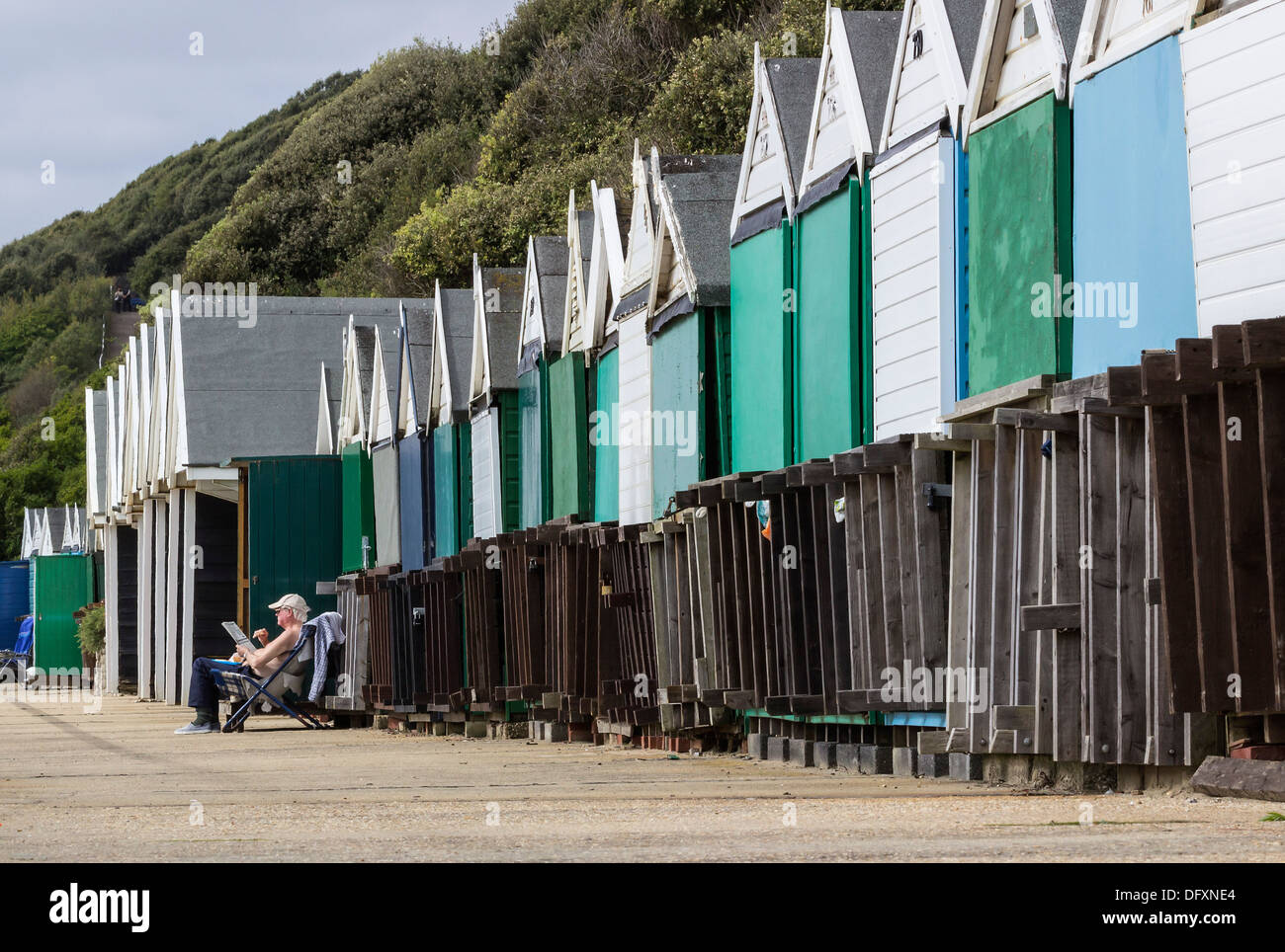 Beach Huts, closed out-of-season, Man relaxing alone in chair on Boscombe Promenade, Dorset, England, UK Europe Stock Photo