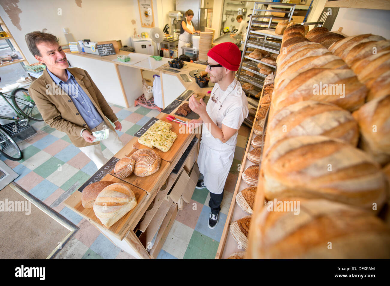 Feature on the Bristol Pound - The East Bristol Bakery, Owner and Head Baker Alex Poulter serves a customer Aug 2013 Stock Photo