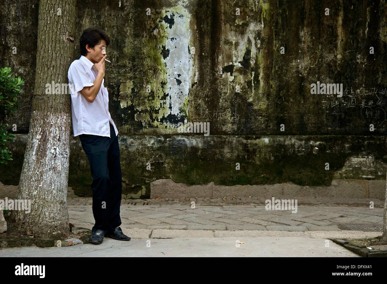Man leaning against a tree smoking, China Stock Photo - Alamy
