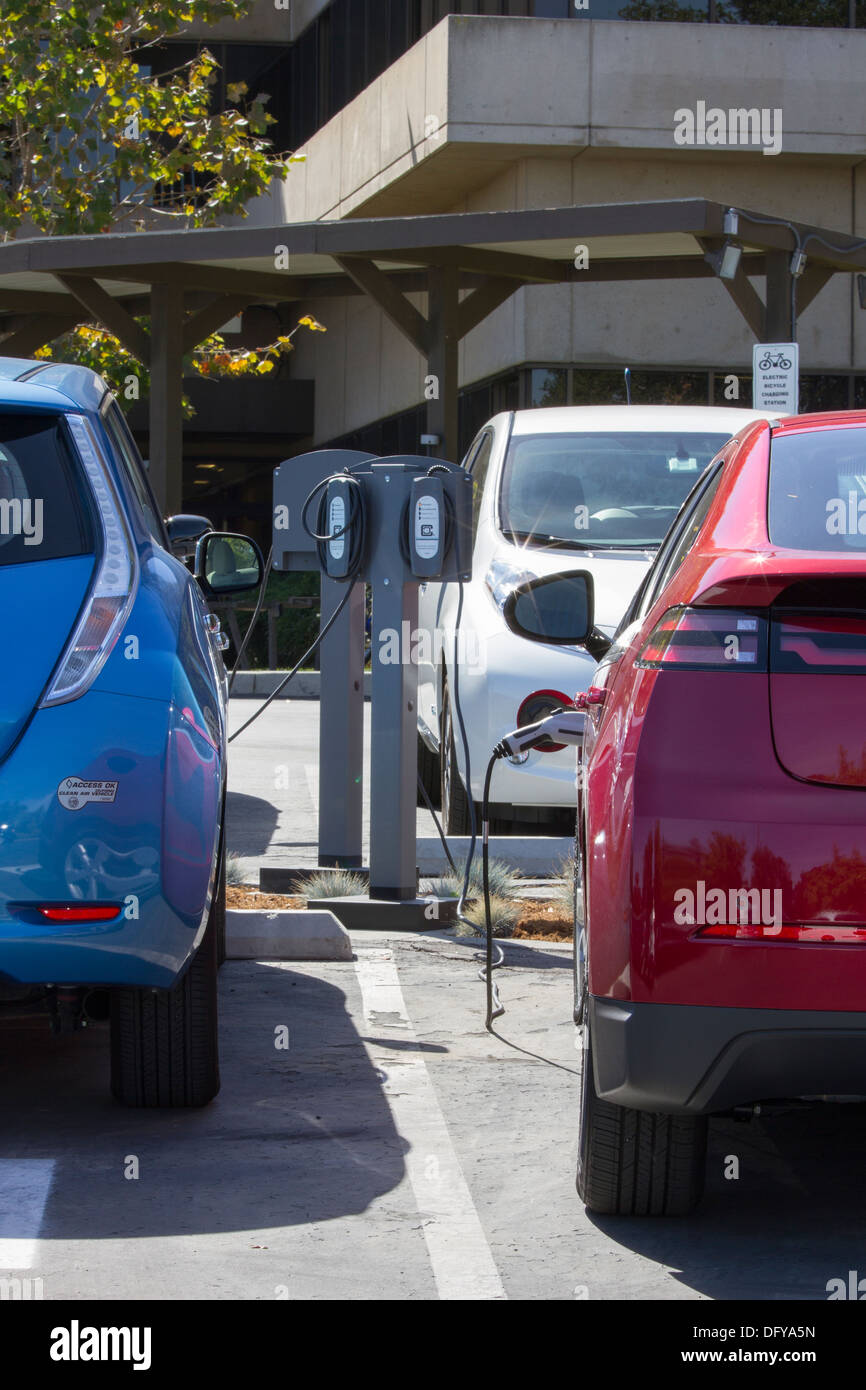 Plug-in electric cars plugged into EV charging stations to charge their batteries in a workplace parking lot Stock Photo