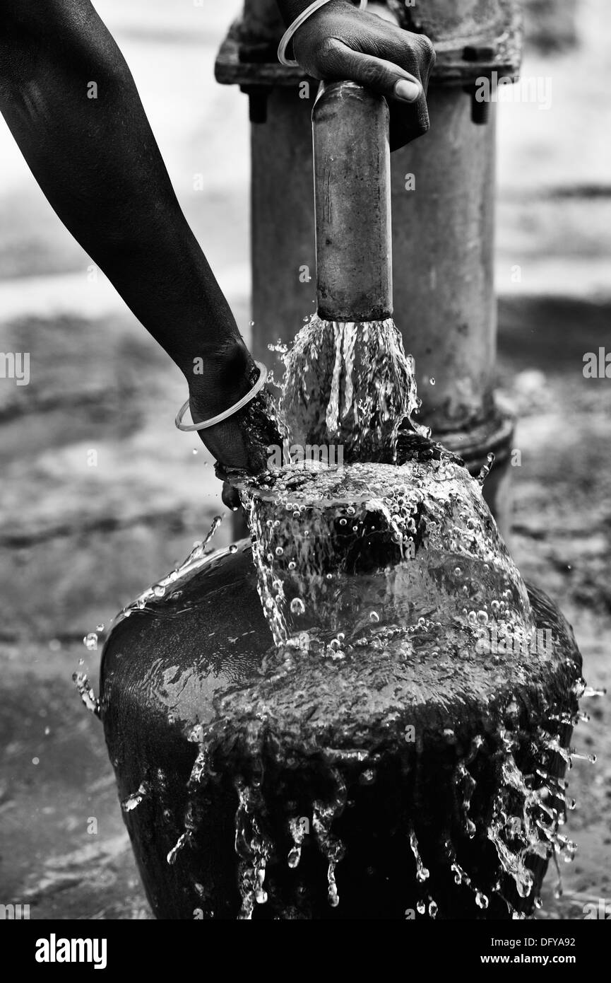Rural Indian woman filling plastic water pot from a rural water pump. Andhra Pradesh, India.  Monochrome Stock Photo