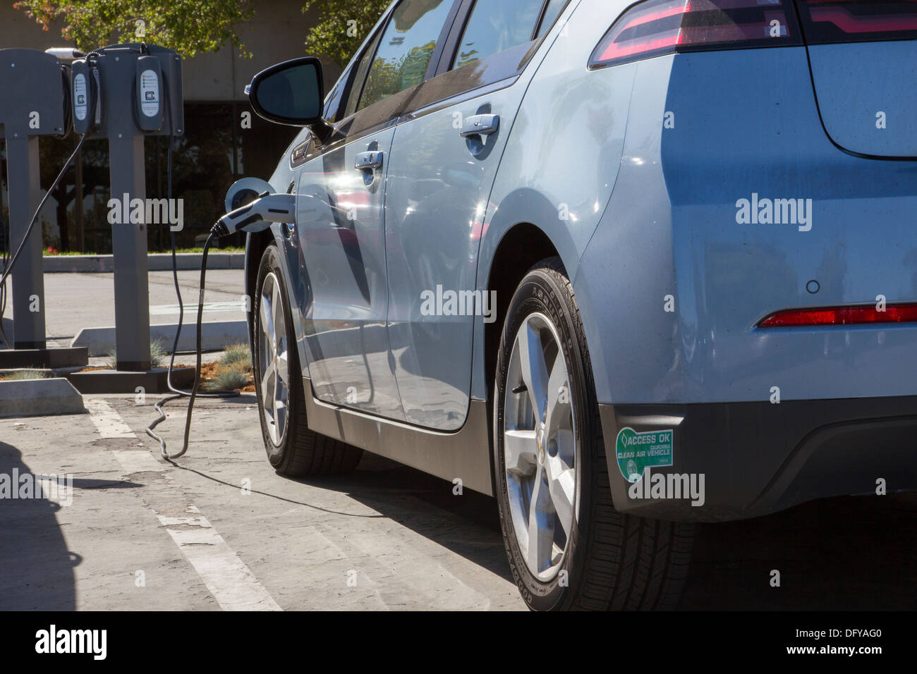 Plug-in electric car with carpool sticker plugged into an EV charging station to charge its batteries in a workplace parking lot Stock Photo