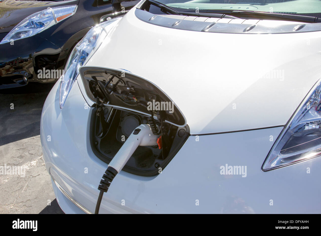 White plug-in electric car with connector plugged into a charging station, charging its battery in a parking lot Stock Photo
