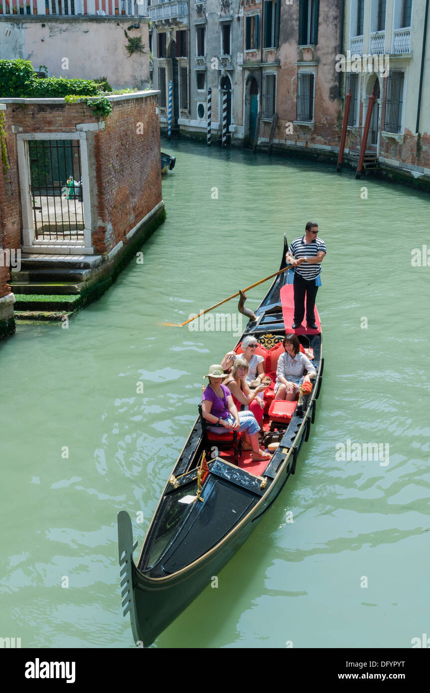 A gondolier ferries female tourists on a gondola through the narrow Venetian canals - Venice, Italy Stock Photo
