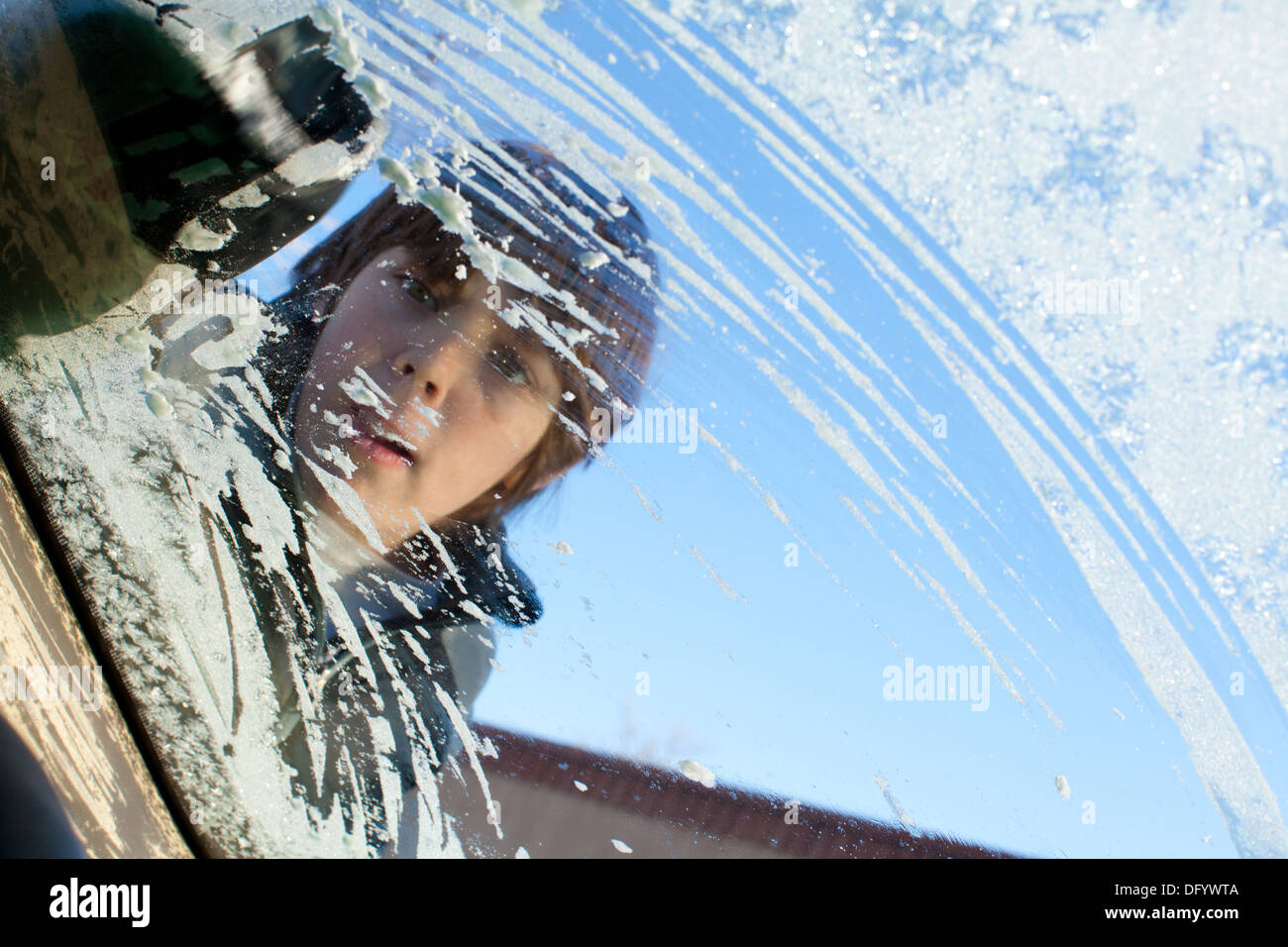 Ten year old boy scrapes ice off of car windshield. Stock Photo