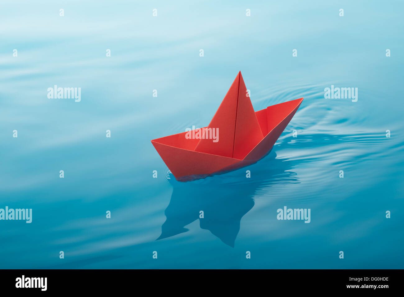 red paper boat sailing on water causing waves and ripples Stock Photo
