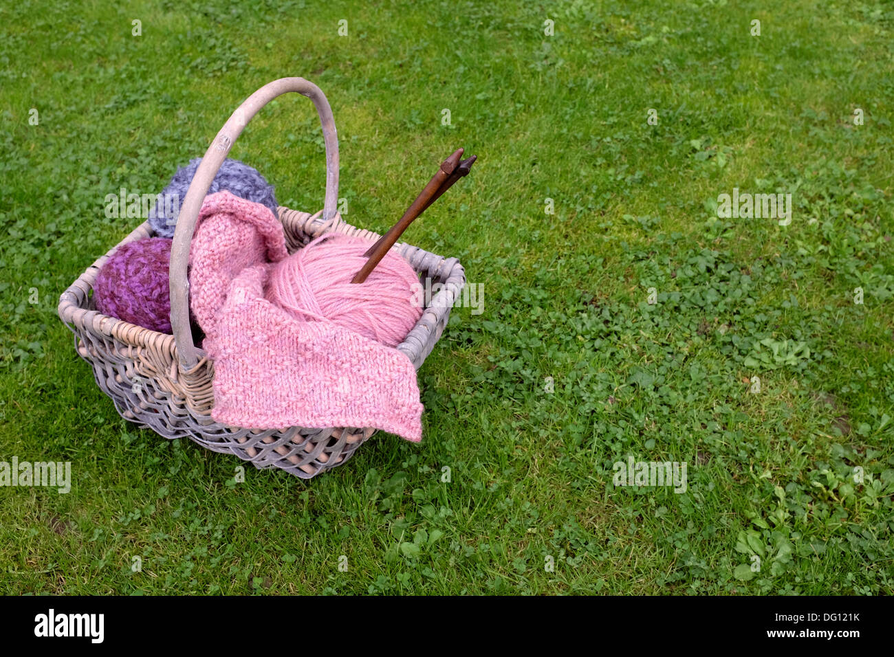 Woven basket of knitting, wooden needles and soft yarn on green grass Stock Photo