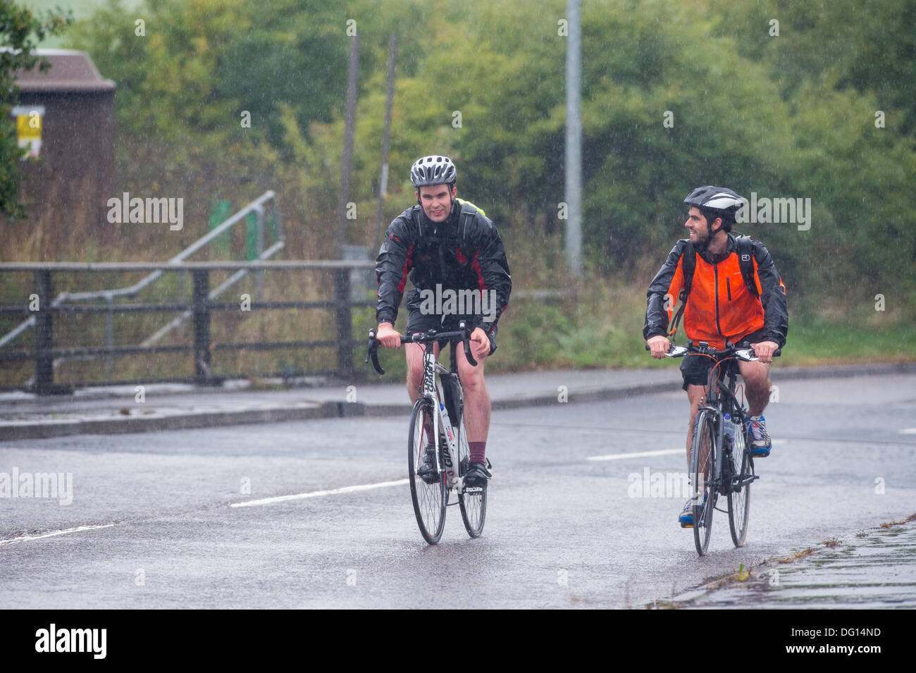 M25 at Brentwood, Essex. 11th October 2013. Weather warnings have been issued for strong winds and heavy rain for parts of the UK. Two hardy cyclists who are cycling from London to The Hague in Holland still manage to find a smile as a soggy and windy journey looms ahead of them. Credit:  Allsorts Stock Photo/Alamy Live News Stock Photo