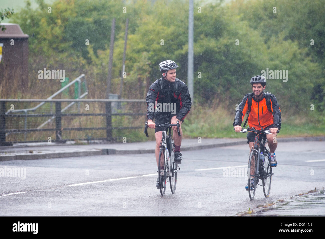 M25 at Brentwood, Essex. 11th October 2013. Weather warnings have been issued for strong winds and heavy rain for parts of the UK. Two hardy cyclists pass above the M25. The pair, who are cycling from London to The Hague in Holland still manage to find a smile as a soggy and windy journey looms ahead of them. Credit:  Allsorts Stock Photo/Alamy Live News Stock Photo