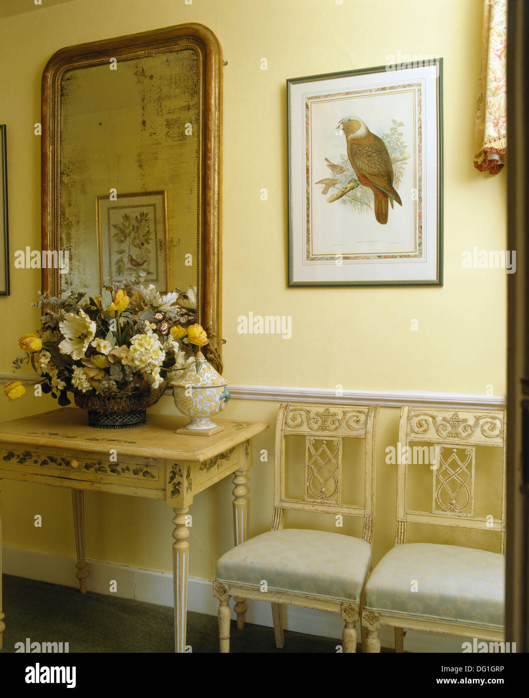 Picture of bird above dining chairs in hall with antique mirror above console table with floral arrangement Stock Photo