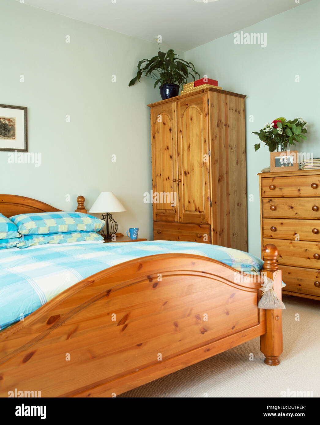 Pine bed with turquoise checked pillows and duvet in economy-style bedroom with pine wardrobe and chest-of-drawers Stock Photo