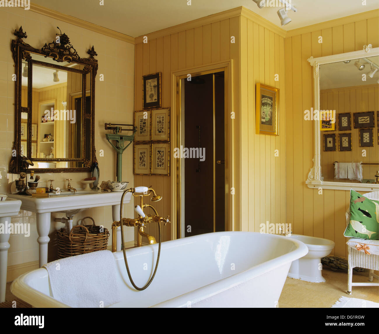 Antique mirror above basin in yellow bathroom with brass shower