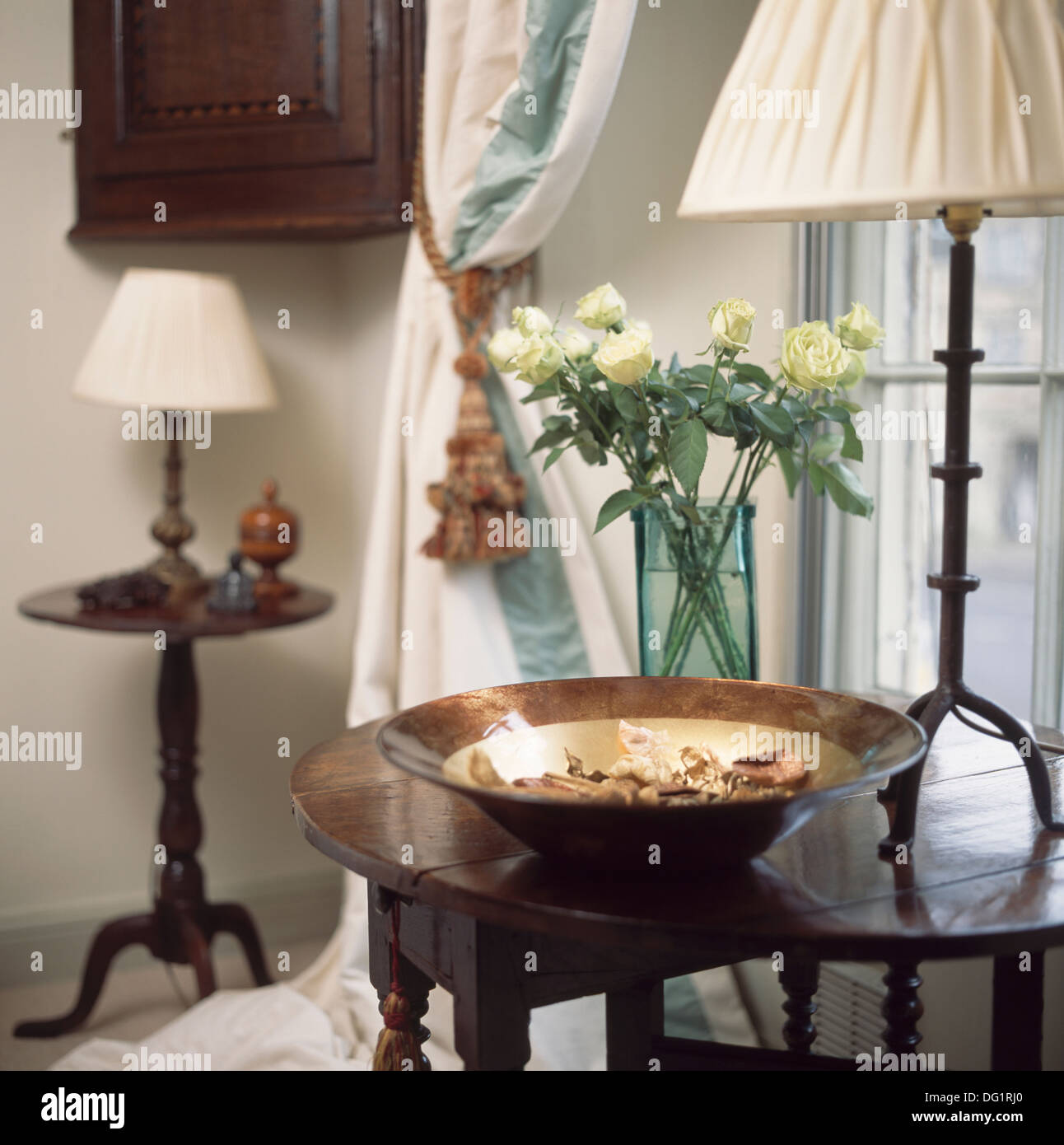 Circular bowl of potpourri and wroughtiron lamp with white shade on antique table in country