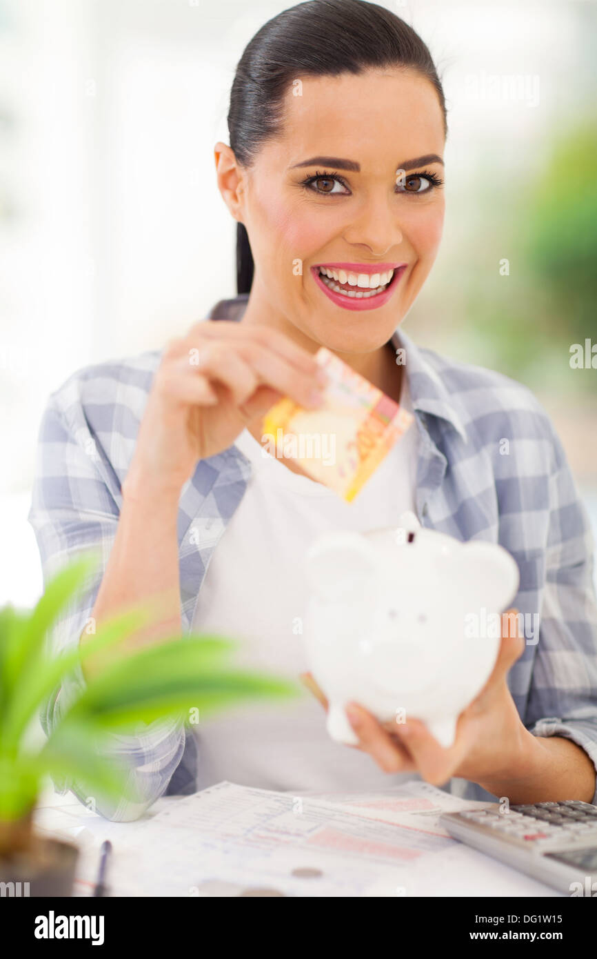 cheerful young woman putting money in piggy bank Stock Photo