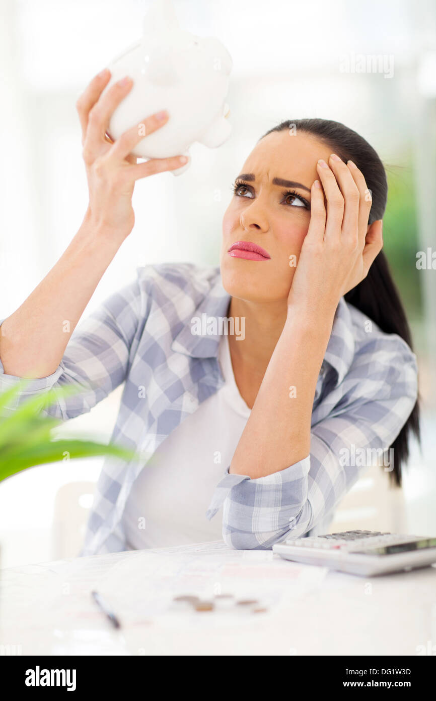 unhappy young woman having financial problems and emptying piggybank savings to pay bills Stock Photo