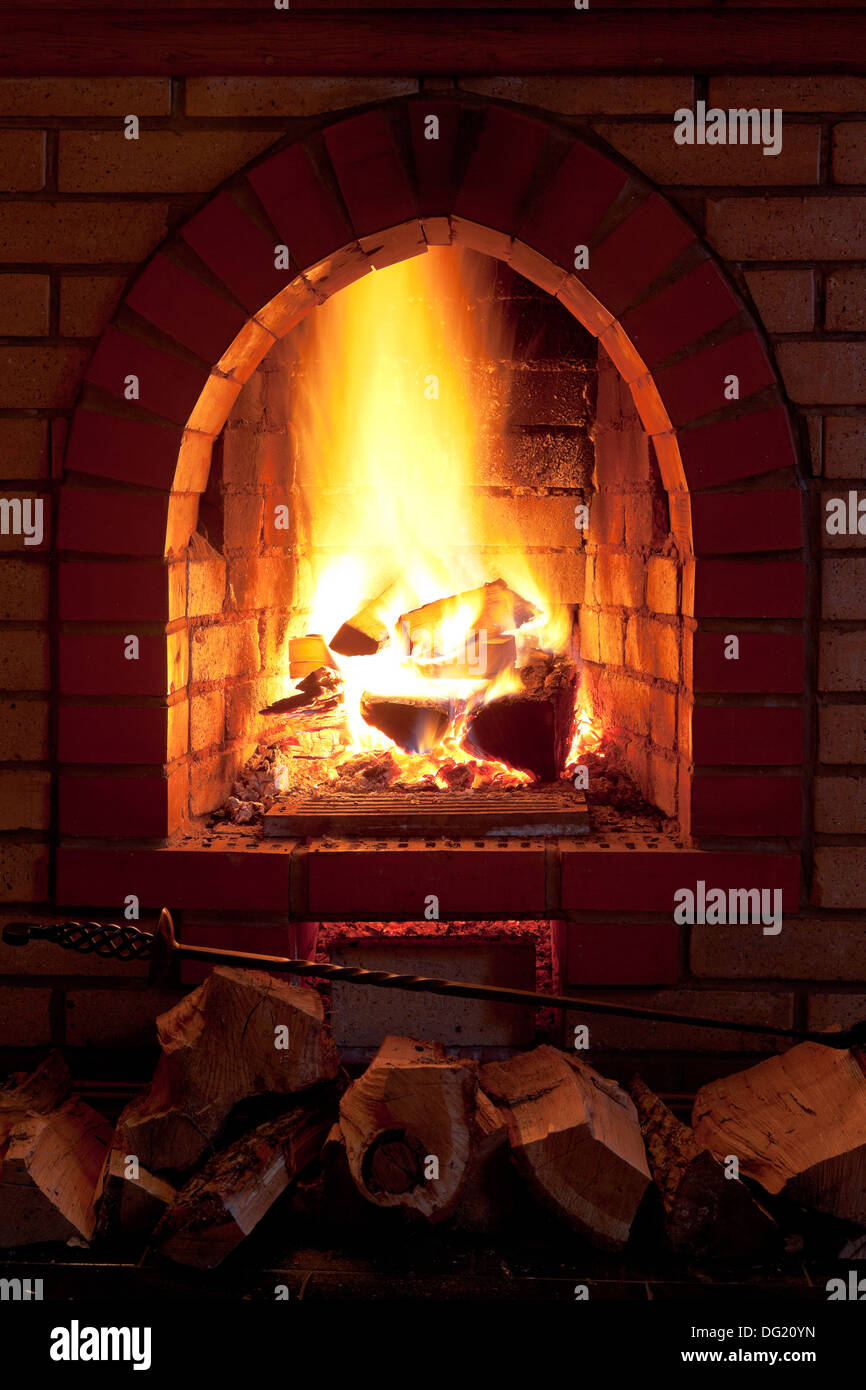 poker, firewood and flames of fire in fireplace in evening time Stock Photo