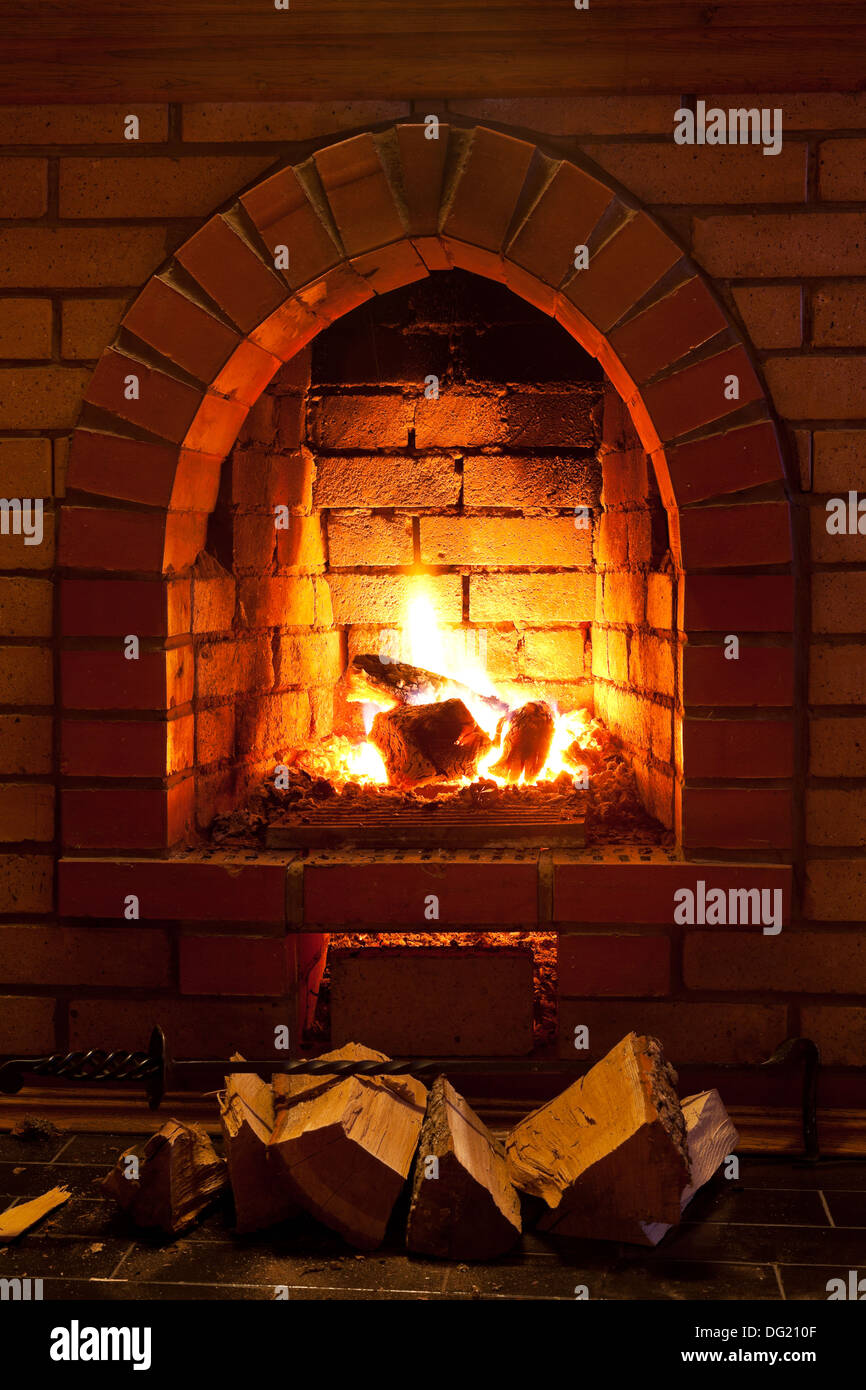 poker, firewood and flames of fire in fireplace in evening time Stock Photo