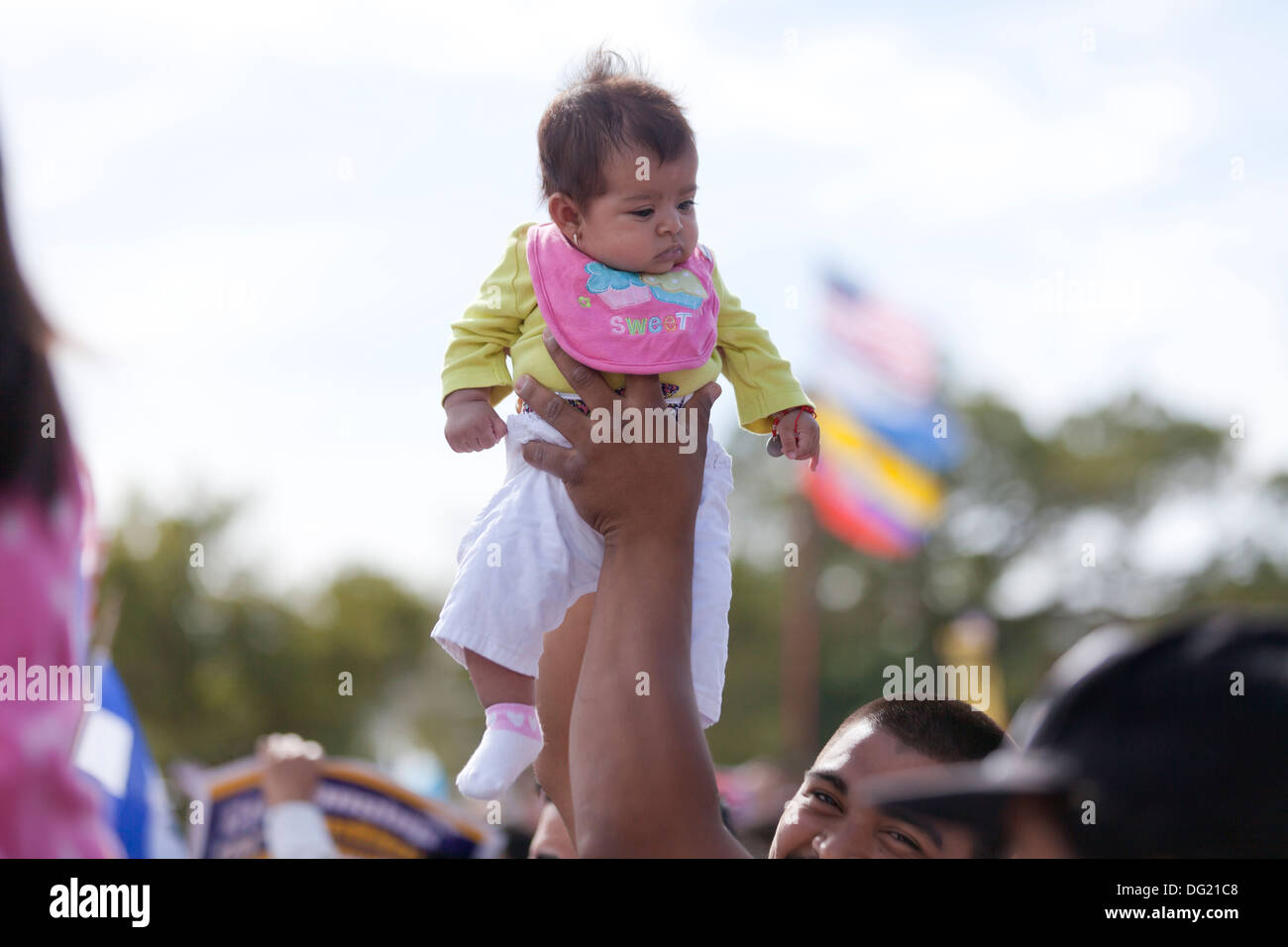 Man holding up infant baby over crowd at an outdoor event Stock Photo