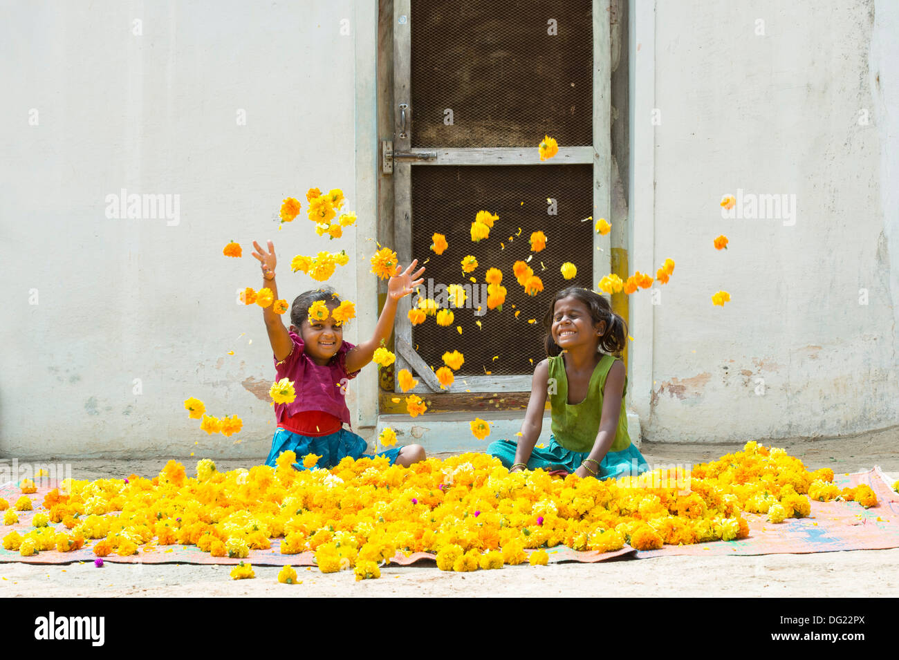 Rural indian village girls playing throwing marigold flowers in the air. Andhra Pradesh, India Stock Photo