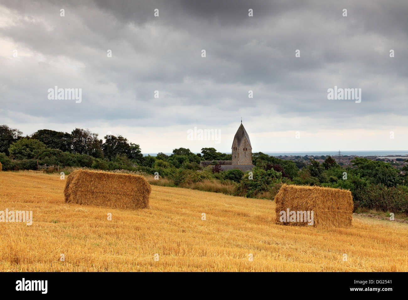 Field of straw bales and St Mary's Church, Sompting, West Sussex. Stock Photo