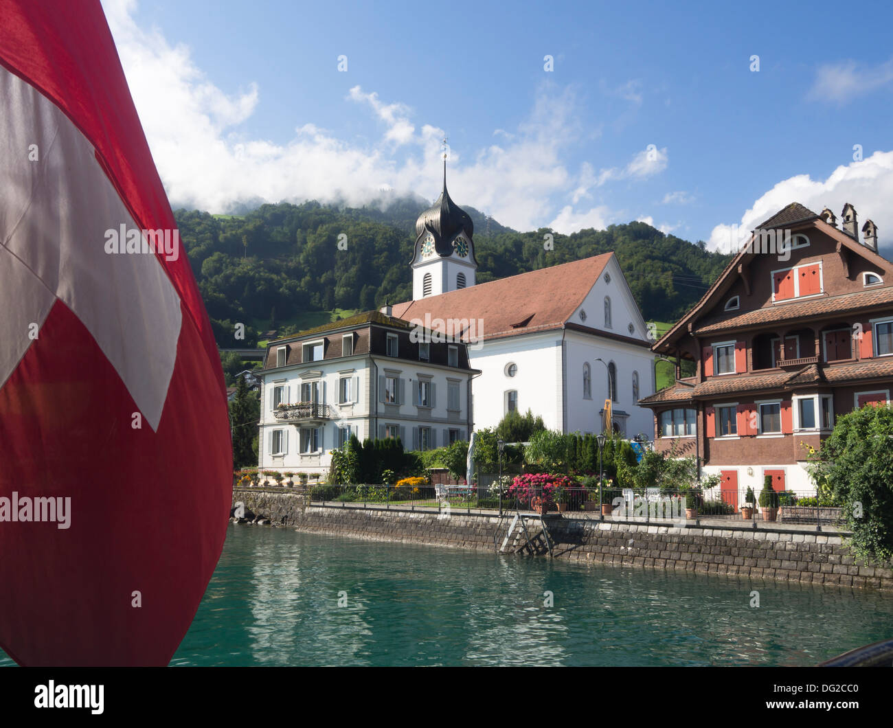 Boat trip on Lake Lucerne Switzerland, leaving Beckenried, church and Swiss flag on stern Stock Photo