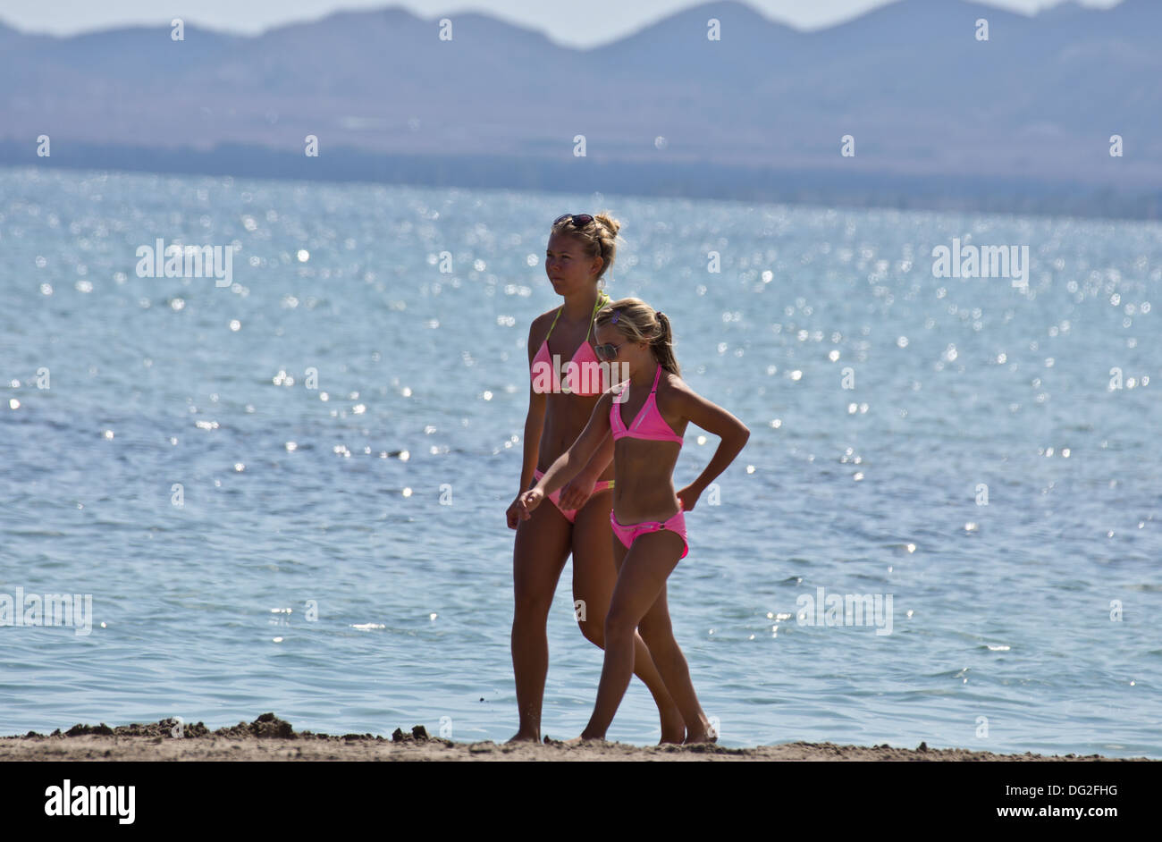 Two young girls  in Pink bikinis walk along the beach together in Los Alcazares Murcia Spain Stock Photo
