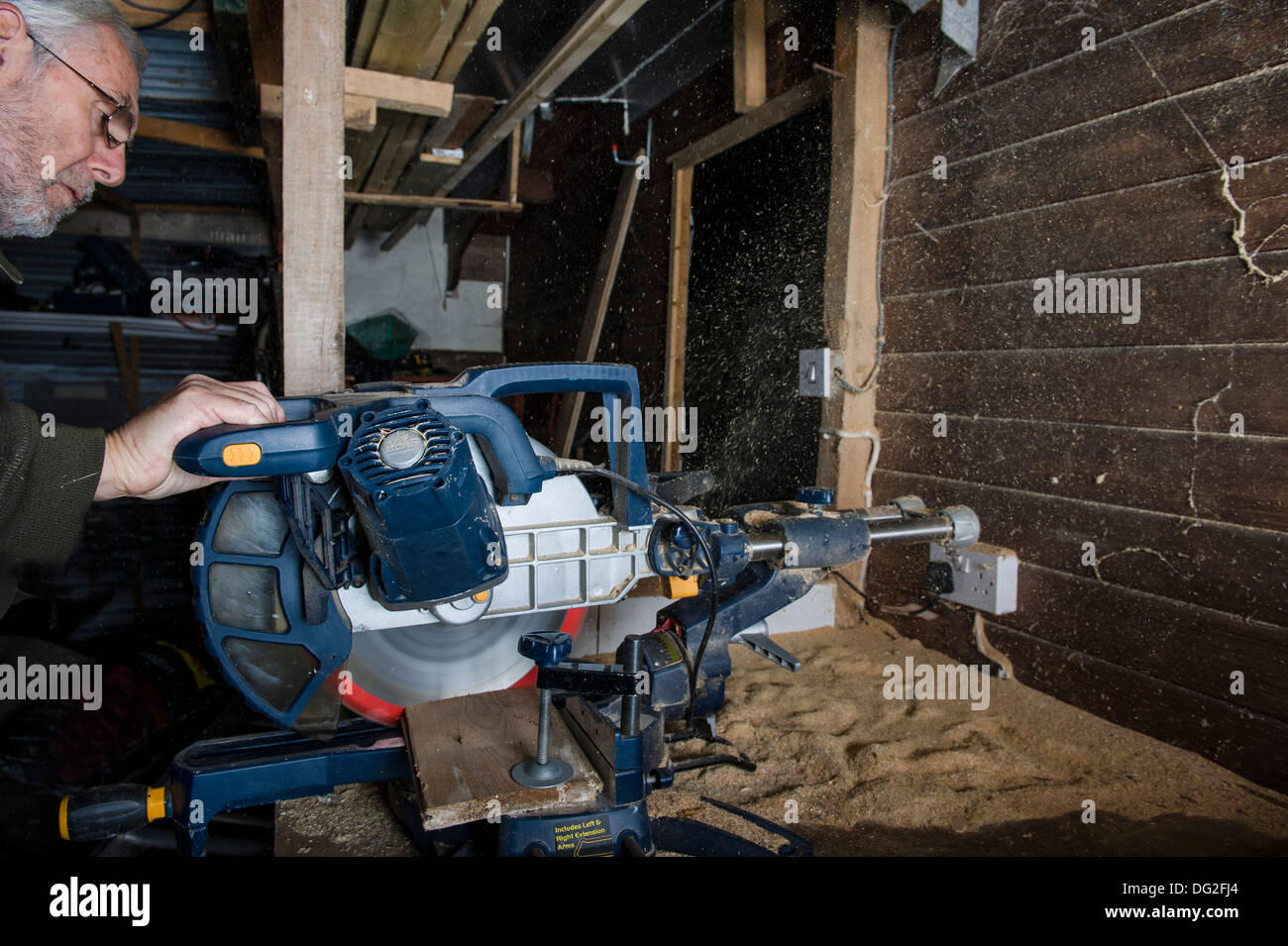 A sliding compound mitre saw, in a workshop, cutting timber with sawdust being ejected from the rear of the saw. Stock Photo