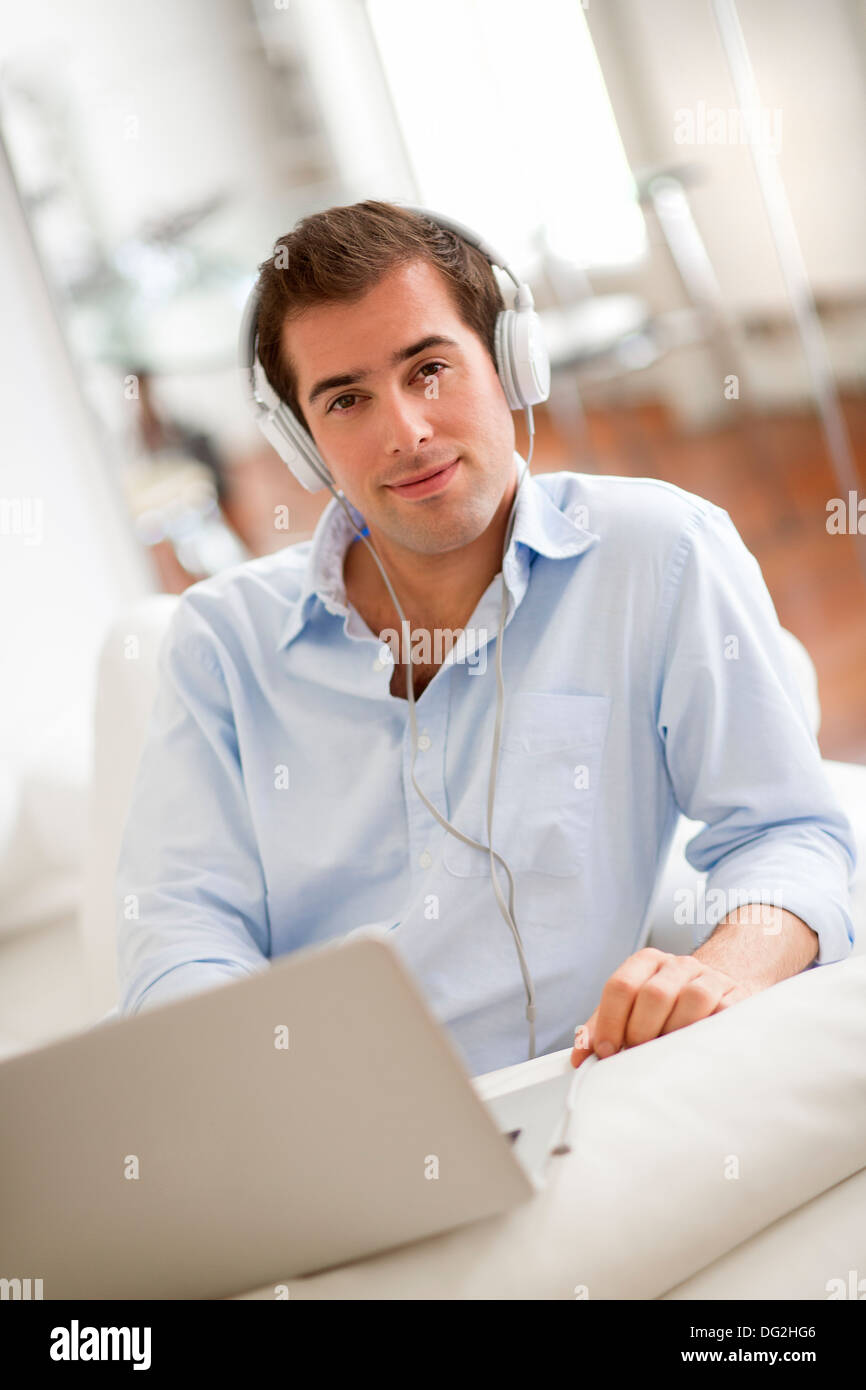Man listening to music with earphones on laptop computer, sitting on sofa Stock Photo