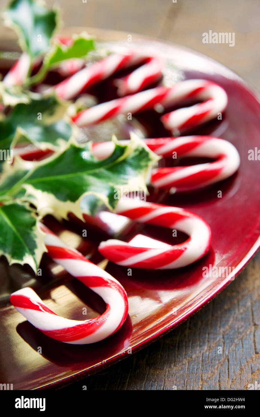 Peppermint candy canes on a plate with holly leaves. Stock Photo