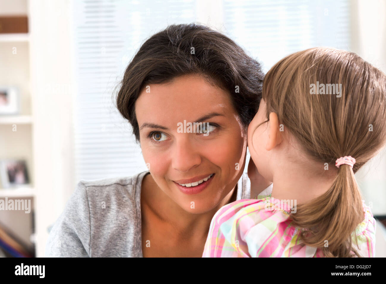 Happy mother with her daughter saying a secret in doors Stock Photo