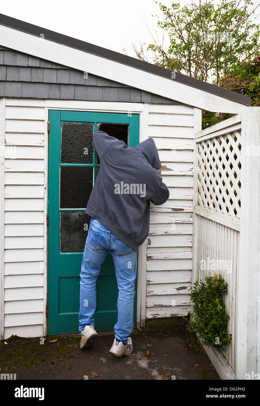 A suspicious person, man wearing a hooded jacket breaking into a garden shed or garage. Stock Photo