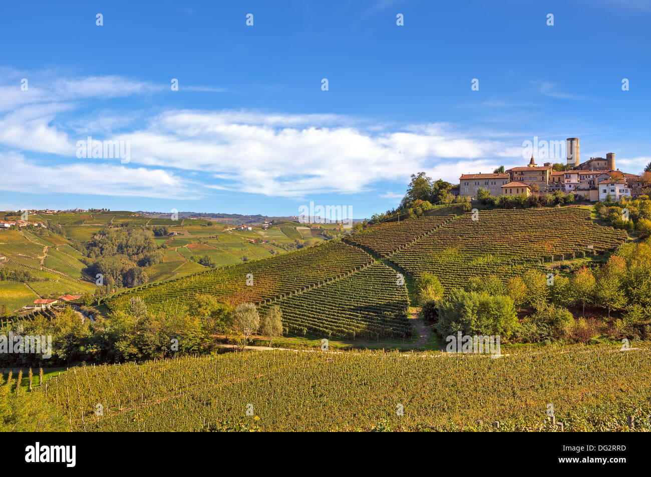 Small typical italian town on the hill over autumnal vineyards under beautiful sky in Piedmont, Northern Italy. Stock Photo