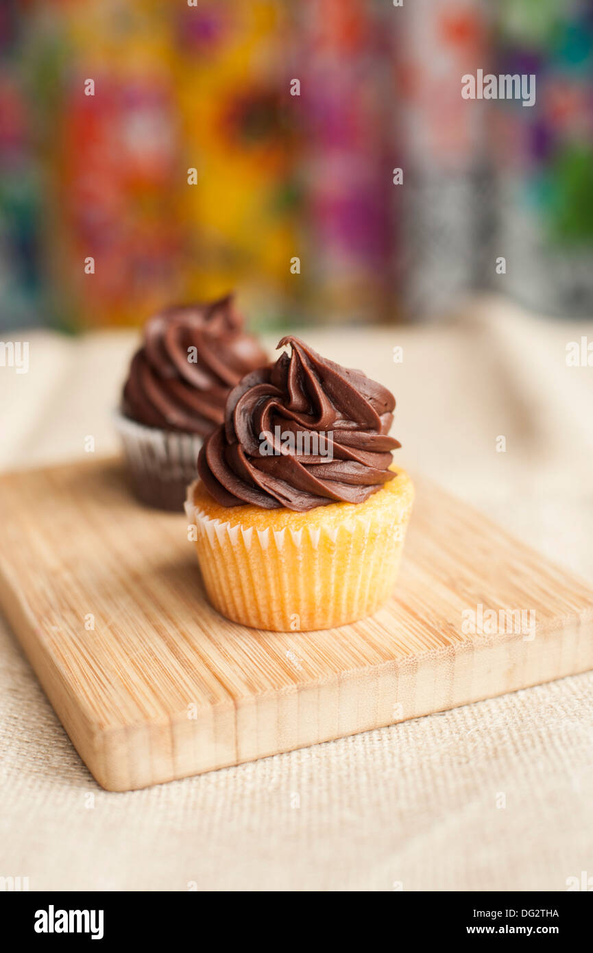 Two Cupcakes with Chocolate Icing on Wood Cutting Board Stock Photo