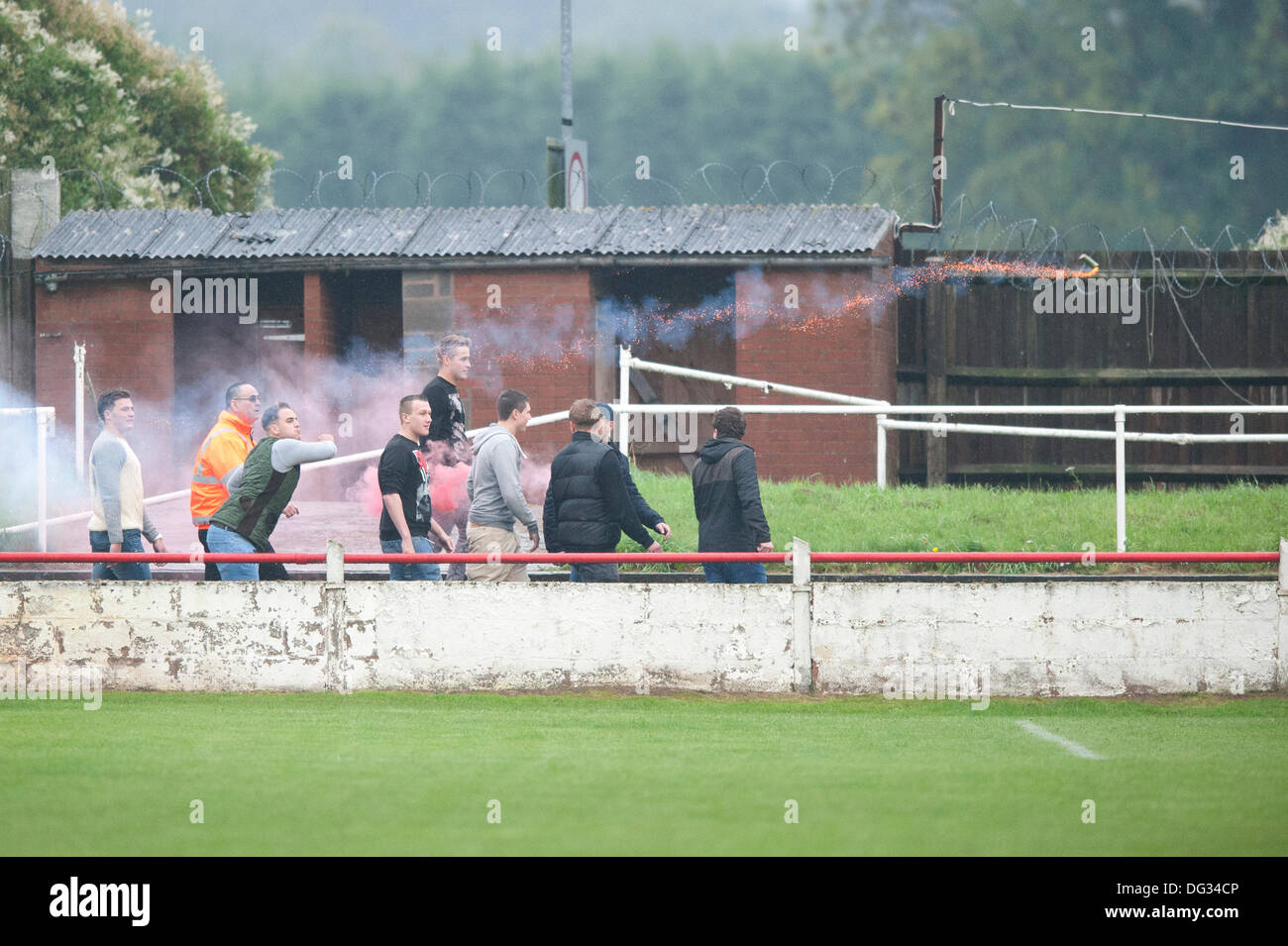 Atherstone, Warwickshire, UK. 12th October, 2013. A group of fans from the home end of the Sheepy Road ground walk around the perimeter of the pitch and scale the fences to attack the visiting supporters (Barrow AFC). A firework was also thrown towards to the terrace of the away following. A flag was stolen from the Barrow AFC fans and then set on fire using a lit firework. Atherstone chairman Rob Weale apologised for what occurred and vowed to pursue the perpetrators. Stock Photo