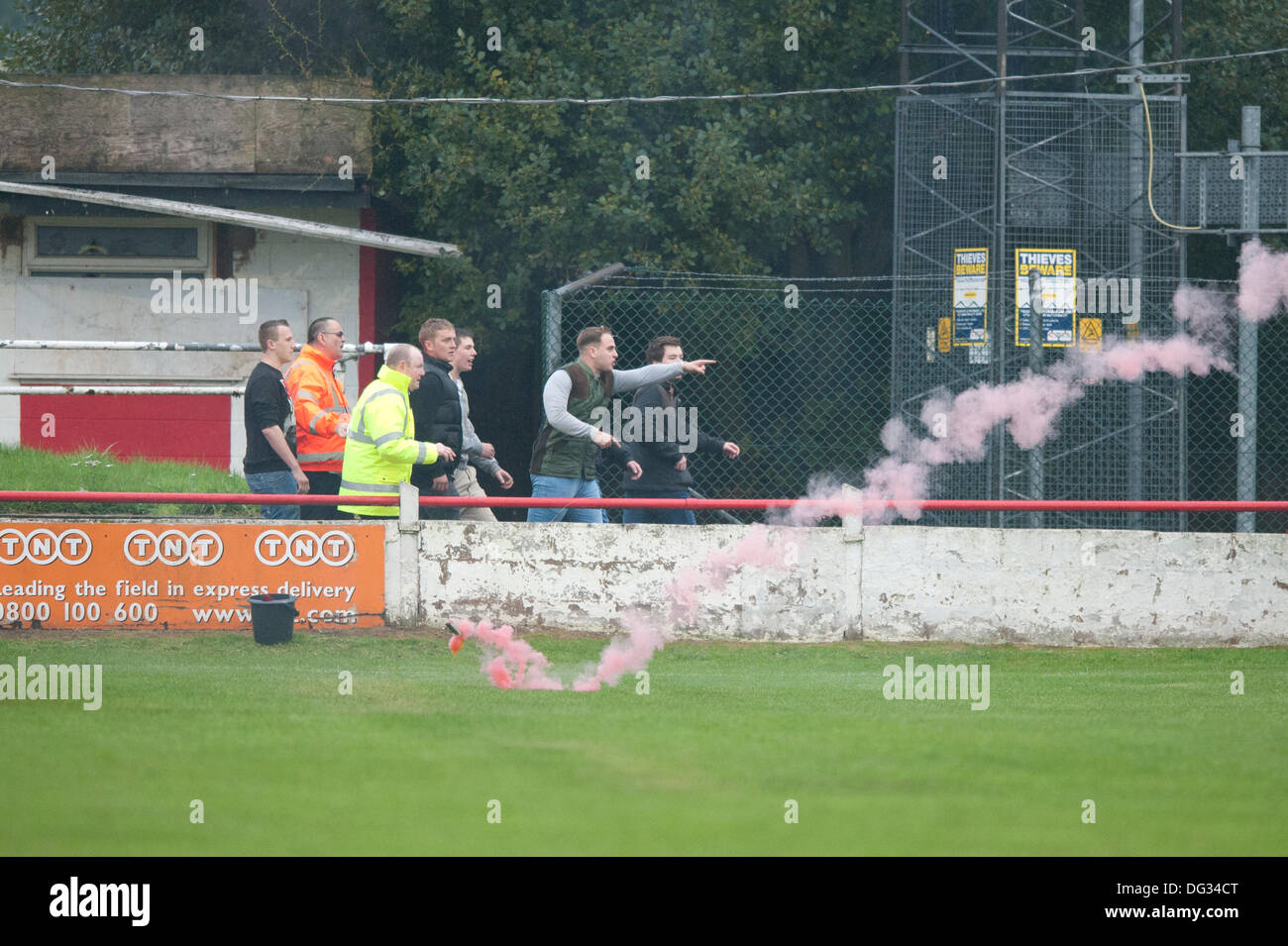 Atherstone, Warwickshire, UK. 12th October, 2013. A group of fans from the home end of the Sheepy Road ground walk around the perimeter of the pitch and scale the fences to attack the visiting supporters (Barrow AFC). A firework was also thrown towards to the terrace of the away following. A flag was stolen from the Barrow AFC fans and then set on fire using a lit firework. Atherstone chairman Rob Weale apologised for what occurred and vowed to pursue the perpetrators. Stock Photo