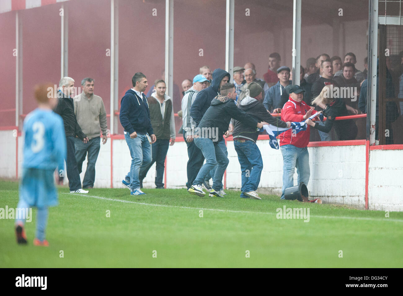 Atherstone, Warwickshire, UK. 12th October, 2013. A group of fans from the home end of the Sheepy Road ground walk around the perimeter of the pitch and scale the fences to attack the visiting supporters (Barrow AFC). A firework was also thrown towards to the terrace of the away following. A flag was stolen from the Barrow AFC fans and then set on fire using a lit firework. Atherstone chairman Rob Weale apologised for what occurred and vowed to pursue the perpetrators Stock Photo