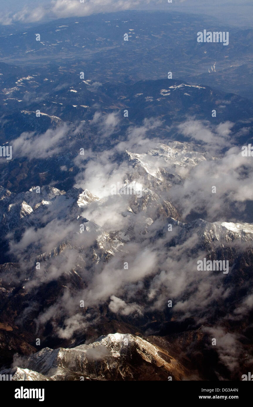 Aerial views of snow clad and rugged rock faced mountains of the Alps with light cloud spread above Stock Photo