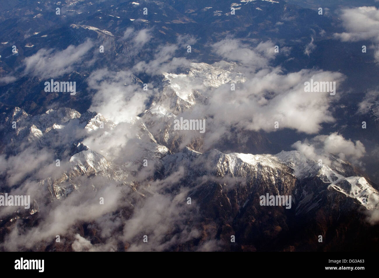 Aerial views of snow clad and rugged rock faced mountains of the Alps with light cloud spread above Stock Photo