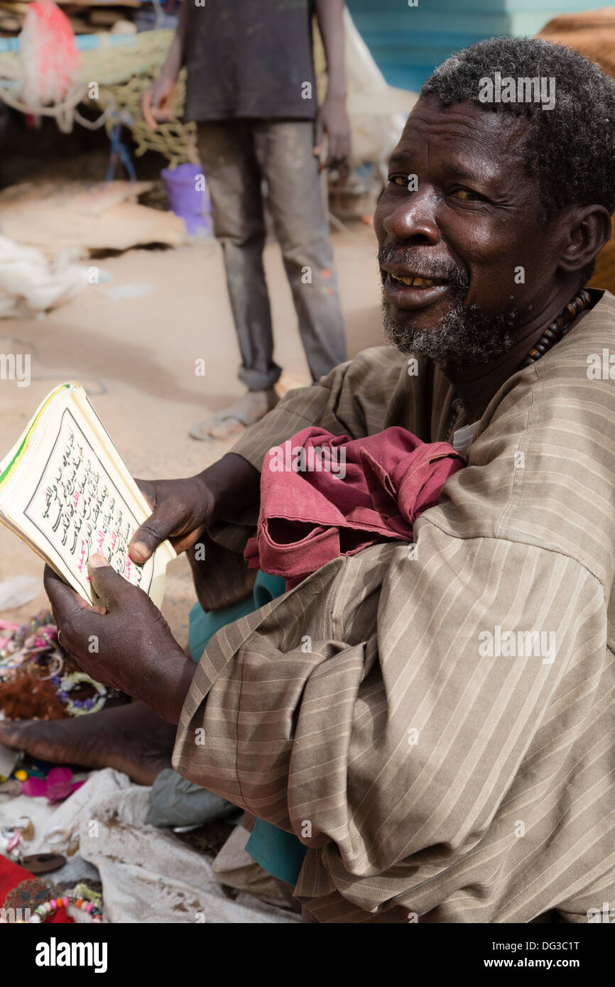 Senegal, Touba. Street Vendor Reading a Booklet in Arabic. Stock Photo